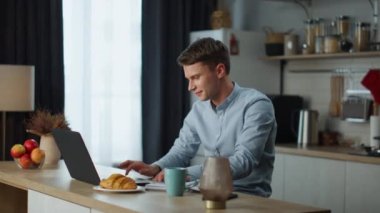 Zoom 'da arkadaşlarıyla sohbet eden olumlu bir adam ev mutfağında oturuyor. İnternet kamerasıyla iş arkadaşlarıyla iletişim kuran mutlu adam. Neşeli adam içeride online sohbet ediyor..