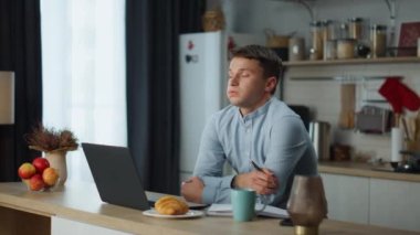 Mutfak masasında oturup iş başarısızlığı endişesiyle dizüstü bilgisayarda çalışan bitkin işadamı. Stresli genç adam projeyi bitirmek için motivasyonsuz işe odaklanamamaktan yoruldu. Serbest çalışan depresyonda..