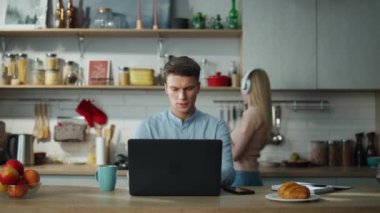 Ciddi derecede meşgul bir yönetici, müşterileriyle mutfakta online zum toplantısı yapıyor. Bu sırada karısı da kahvaltı hazırlıyor. Genç çekici iş adamı evdeki video konferansında konuşuyor. Uzak çalışma konsepti.