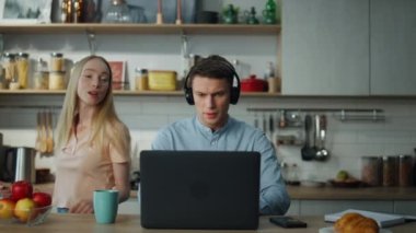 İnternette müşteriyle konuşurken kulaklık takan yakışıklı bir internet danışmanı. Odaklanmış yönetici dizüstü bilgisayarda yakınlaştırma konferansı düzenlerken mutlu kadın arka planda dans ediyor..