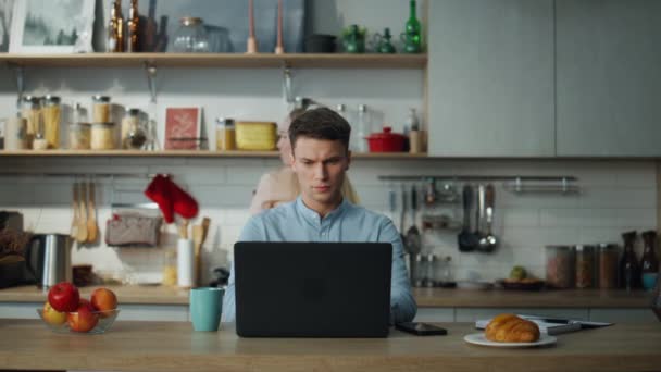 专注于在笔记本电脑上工作的创意作家喝咖啡 年轻活跃的女人戴着耳机在丈夫的电脑上跳舞 冷静严肃的男人看着银幕上无视快乐的妻子 — 图库视频影像