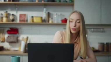 Serbest çalışan kız dizüstü bilgisayarda ders alıyor. Not defterine yakın çekim notlar alıyor. Mutfak masasında oturmuş Webinar eğitimi alan çekici bir kadın. Uzaktan çalışan güzel sarışın bayan..