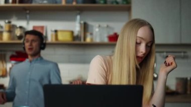 Çekici bir kadın internette danışmanlık yaparken, erkek arka planda kulaklıkla müzik dinlerken mutfağa video çağrısı yapıyor. Zoom konferansında konuşan kendine güvenen iş kadını uzaktan yakından çalışıyor..