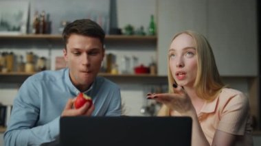 Modern mutfakta dizüstü bilgisayar kullanarak sanal toplantıdan hoşlanan pozitif bir çift. Arkadaşlarıyla görüntülü görüşme yapan mutlu bir kadın. Evli çiftler web kamerasında gülümsüyor..