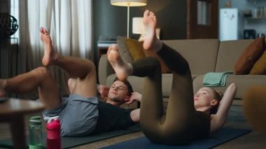 Evli çiftin karın kasları dairede bisiklet gibi döner bacaklarla yatıyordu. Ayaklarını kaldıran genç bir kadın sağlıklı bir adamla karın kasları için egzersiz yapıyor. Genç aile sağlıklı vücutla ilgileniyor..