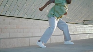 Esnek erkek bacakları, merdivenleri yakın çekimde dans ediyor. Bilinmeyen Afro-Amerikan adam şık kıyafetler içinde etkileyici danslar yapıyor. Çirkin arka planda serbest stil pratiği yapan isimsiz bir sanatçı. Gençlik kültürü