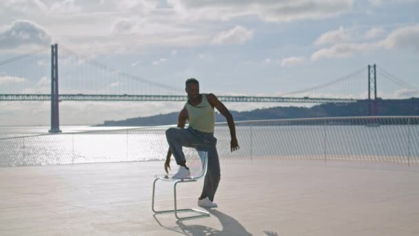 ファッションマンは椅子だけで踊る 海を背景にコンテンポラリーダンスのパフォーマンスを披露する現代のパフォーマー 海の見える場所で新しい技術をリハーサルするアフリカ系アメリカ人の男 青少年文化の概念 — ストック動画