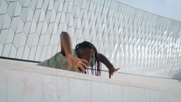 抽象的な建物の近くに体を動かす精力的な男 都市空間でコンテンポラリーダンスの要素を見せるアフリカ系アメリカ人 柔軟なドレッドロックダンサー1人で演奏 創作アートのコンセプト — ストック動画