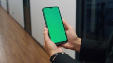 Yakın çekim elleri, krom ekranlı akıllı telefonu tutuyor. Ofiste yürüyen yönetici görüntülü konuşma yapıyor. Online platformun şablonunu izleyen tanınmamış bir kadın çalışıyor. Teknoloji yaşam tarzı konsepti