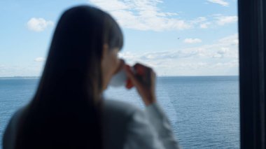 Silhouette woman tasting coffee at ocean view closeup. Businesswoman having espresso cup rest at panoramic window luxury hotel. Anonymous leader person overlooking sea horizon after working day 