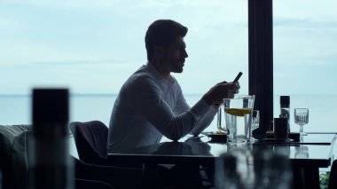Busy businessman using smartphone on lunch in luxury restaurant. Focused freelancer working online on mobile phone device in cafe. Handsome employee reading corporate message on cellphone profile. 