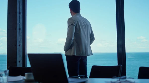 Serious businessman watching sea window back view. Confident leader person waiting walking alone modern company luxury office. Director thinking planning at corporate building conference room