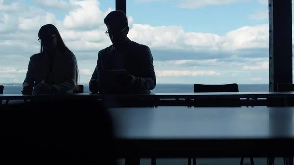 Two silhouettes working sea viewin office. Business partners checking documents financial report. Unrecognized businessman analyzing preparing agreement with secretary manager. Couple signing contract