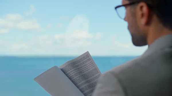 Businessman reading papers at ocean view hotel closeup. Focused entrepreneur man checking documents at panoramic window office. Serious director analyzing financial data statistics at remote workplace
