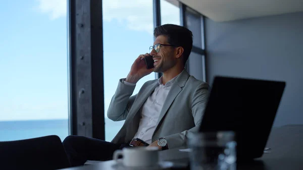 Smiling businessman talk smartphone at marine landscape workplace. Man professional having conversation on cellphone in sea view office. Joyful boss director call phone in panoramic window interior