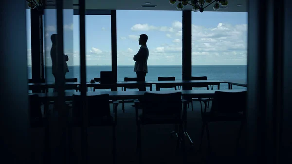 Businessman silhouette enjoying break in conference room. Calm beautiful sea view. Unrecognized man ceo thinking life problems dreaming in office alone. Peaceful manager entrepreneur having pause