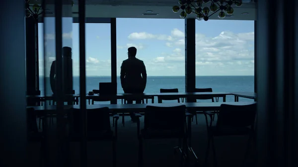 Ceo man silhouette thinking sea panorama window. Confident corporate professional worker resting at ocean view hotel. Leader person looking at water cloudy sky horizon. Business lifestyle concept