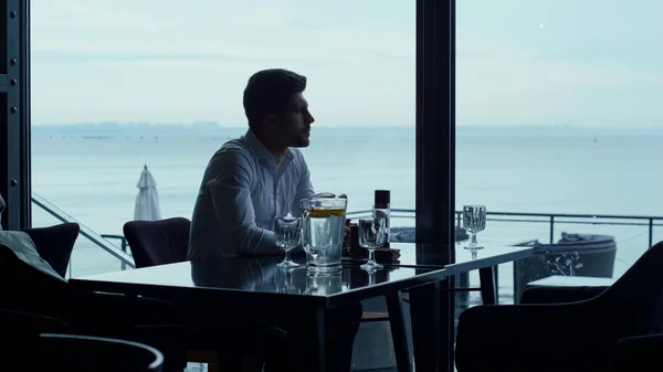Stressed man silhouette spending breakfast in panoramic cafe alone. Thoughtful businessman looking ocean view in hotel restaurant. Rich manager resting lunch break in luxury bar. Loneliness concept.