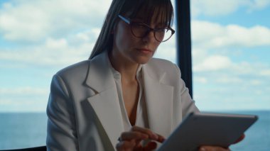Çevrimiçi güzel bağımsız çalışma projesi. Odaklanmış yönetici panorama penceresinde tablet sörfü yapıyor. Çekici esmer iş kadını dijital ped kullanarak mali raporları kontrol ediyor..