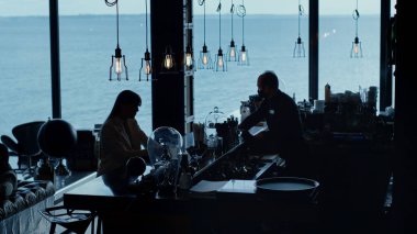 Çaresiz iş kadını silueti kokteyl okyanus manzarası içiyor. Barmen panoramik pencerelerde oturan meçhul kadın. Karanlık otel. Restoranda tek başına çalışmaktan yoruldun. Kişisel kriz konsepti