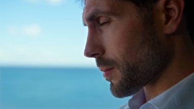 Tired man face rubbing eyes at sea view office closeup. Portrait of bearded exhausted entrepreneur in panorama window luxury hotel room. Unshaven unhappy lawyer feeling headache portrait 