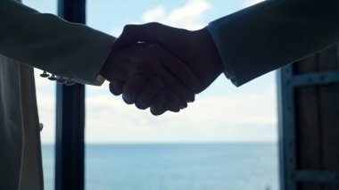 Ortaklar el sıkışıyor okyanus manzaralı yakın çekim. İş dünyasının siluetleri başarılı bir iş birliğini kutluyor. Tanımlanamayan yönetici, lüks konferans odasında müşteriyi selamlıyor. Anlaşma kavramı 