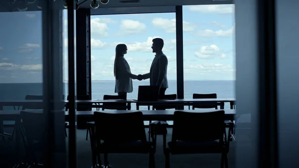 Partners silhouettes shaking hands at marine view. Business team taking seats discussing successful deal cooperation. Unrecognized manager consultant greeting client new coworker in conference room.
