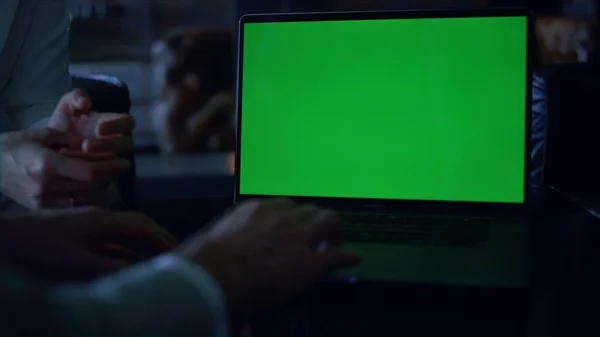 Coworkers hands using chroma key laptop closeup. Unknown entrepreneurs team working online on green screen computer at dark office interior. Unrecognizable business couple meeting with mockup device