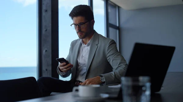 Focused businessman checking documents in sea view office interior. Man worker answering on phone ring. Director talking smartphone at panoramic window workplace. Leader person calling at hotel