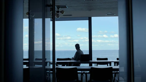 Businessman silhouette resting sea dark office. Company intern looking window taking break in luxury conference room. Unrecognized worker manager contemplating project issues enjoying marina landscape