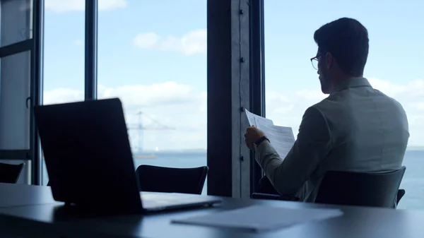 Office manager checking documents at panorama window rear view. Man read papers at sea panorama window. Unknown businessman finance expert working holding company report. Investor analyzing deal.