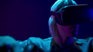 Professional gamer exploring environment in simulation closeup. Young generation z man in VR helmet using wireless controllers playing at neon light. Modern technologies and metaverse concept