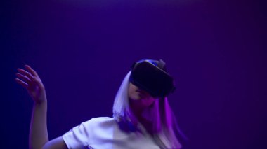 Millennial girl dancing moving metaverse game closeup. Woman getting experience using VR headset glasses in neon multi coloured place. Youngster gamer playing enjoying 3D simulation alone slow motion