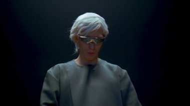 Yakın planda fütürist gözlük takan adam. Fütürist oyuncu karanlık arka planda sanal nesneler seçiyor. Blonde Millennial Man yüksek teknoloji gözlükleriyle gelişmiş gerçekliği tecrübe ediyor..