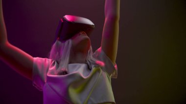 Closeup excited woman experiencing VR headset videogame. Impressed gamer using gadget for virtual reality on neon background. Futuristic goggles girl playing controllers. Future technology concept 