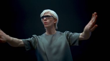 VR elemanı simülasyonu fütüristik kıyafete yakın çekime sokuyor. Odaklanmış oyuncu karanlık arka planda çevrimiçi metaevren dünyasına giriyor. Büyütülmüş gerçekliği keşfeden gelecekteki sarışın adam. Merhaba teknoloji yenilik konsepti.