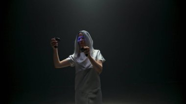 Çekici kız dijital gözlüklerle arttırılmış gerçeklik oynar. Metaverse oyuncular ışıktaki konsol kontrolörlerini kullanarak simülasyondan zevk alırlar. İnteraktif siber uzaya dalan fütürist sarışın. Akıllı gelecek konsepti