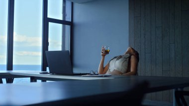 Tired manager drinking whiskey in office. Stressed woman relaxing with alcohol alone. Depressed ceo freelancer feeling sad considering personal health issues. Thoughtful businesswoman overworking.