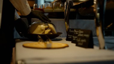 Closeup hands setting glass bell dome on breakfast bakery buffet. Unknown waiter closing dish plate. Black table nameplate standing on restaurant counter close up. Dark interior in modern lounge cafe.