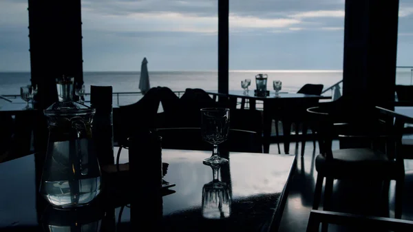 Evening sea view in stylish restaurant dining hall background. Served event tables in cozy lounge hotel bar. Premium business lunch tableware in dark cafe interior. Contemporary cafeteria design.