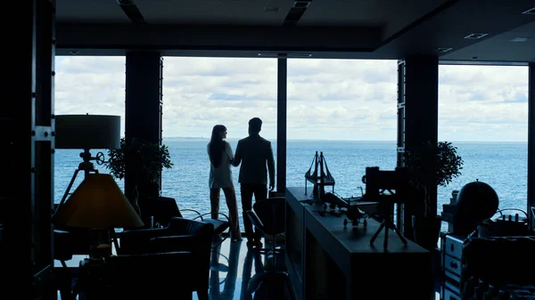 Dark silhouette colleagues meeting panoramic window workplace. Executive greeting woman boss at luxury ocean view office. Unrecognizable business team working together. Corporate lifestyle concept