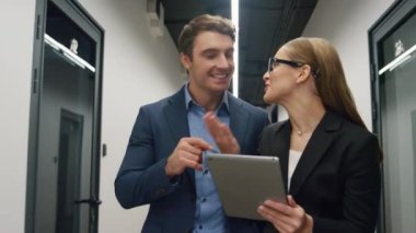 Gülümseyen işçiler tablet raporlarını kontrol ediyor. Başarılı proje hakkında konuşan etkileyici iş adamları ofis merkezinde yürümeyi başarıyor. Mutlu yönetim ekibi tarama verilerine seviniyor. Kurumsal zafer kavramı
