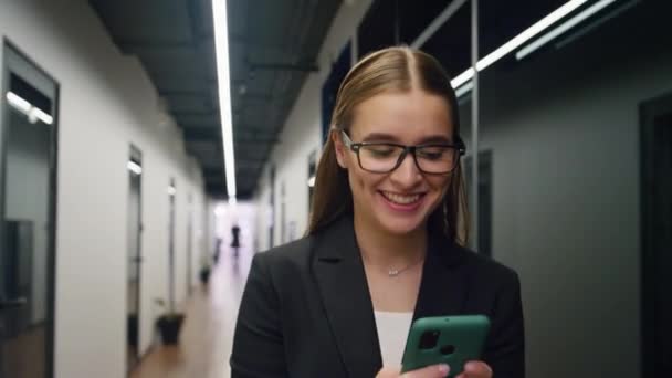 スマートフォンのメールをチェックする幸せなビジネス女性 笑顔のマネージャーはいジェスチャー良いニュースを読んでください 外出先で携帯電話を使用して喜んで成功した研修生 美しいオフィス従業員は仕事の昇進を得る — ストック動画