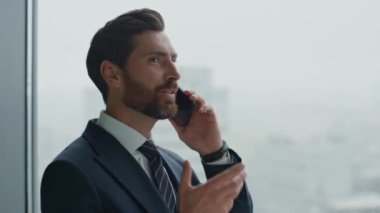 Mutlu sakallı ofis çalışanının portresi telefonda konuşup pencereye gülüyor. Çekici, kendine güvenen iş adamı iş arkadaşlarıyla telefonda konuşmaktan zevk alıyor. Yönetici gülümsüyor, iyi haberler geliyor.