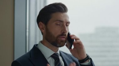Mali danışman ofisin panoramik penceresinde telefonla konuşuyor. Modern akıllı telefonu kullanarak müşteri danışmanlığı. Kendine güvenen sakallı iş adamı telefon görüşmesi yapar..