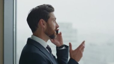 Gülümseyen başarılı yönetici, panoramik pencerenin önünde duran iş arkadaşlarıyla telefon görüşmesi yapıyor. İş anlaşmasını telefonla sonuçlandıran mutlu iş adamının portresi..