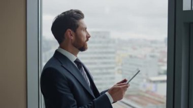 Başarılı, kendine güvenen patron tablet tutuyor. Şirketin başarısına seviniyor. Finans raporunu yakından okuyor. Çekici sakallı iş adamı ofis penceresinin yanında bilgisayarla ayakta durmaktan mutlu..