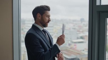 Ofis penceresinde kağıt uçak tutan düşünceli yönetici şehir manzarasına yakından bakıyor. El yapımı origami yapmayı düşünen düşünceli ve zeki bir iş adamı..
