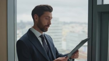 Düşünceli orta yaşlı yönetici ofis penceresinin yanında duran iş belgesini kontrol ediyor. Ciddi iş adamı borç bildirimi konusunda stresli hissediyor. Depresyondaki adam yüksek faturalardan usanmış..