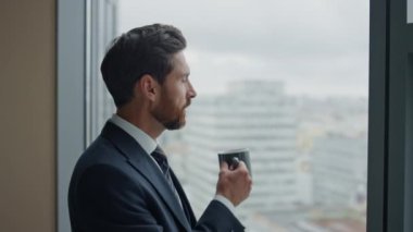 Ofis panoramik penceresinde kahve içen düşünceli işadamının yan görüntüsü. Düşünceli sakallı CEO 'nun portresi. Şehir görüşüne bakıyor. İş görüşleri düşünüyor, kararlar veriyor.